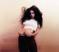 Charlie XCX en débardeur blanc adossé contre un mur